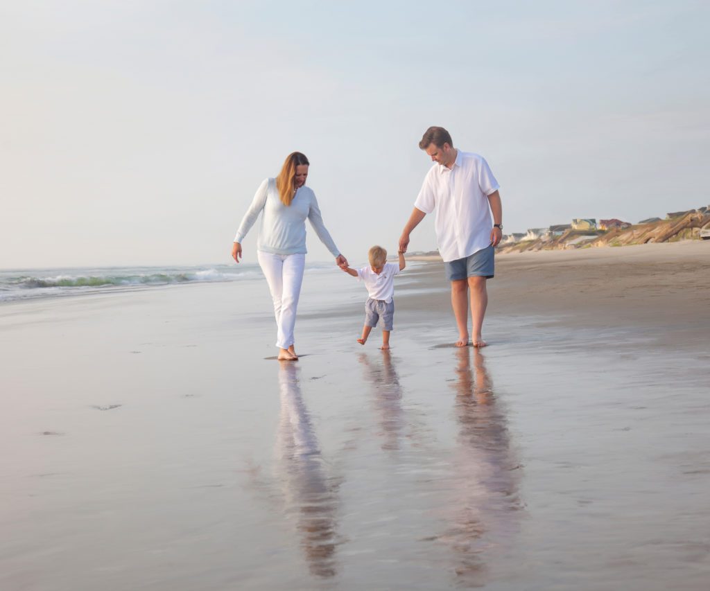 a photo of a baby and parents walking on the beach in Corolla NC