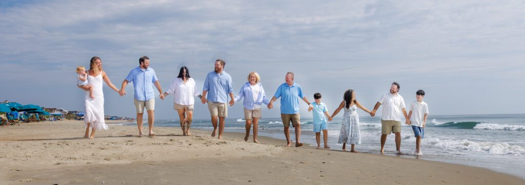Extended family walking hand-in-hand during a sunrise beach portrait session in Corolla, North Carolina, photographed by Certified Master Photographer Bruce Lorenz.